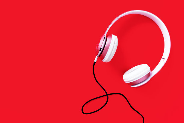 粉色耳机和黑色电缆在柔和的颜色红色背景。音乐的概念。空白空间复制素材图片