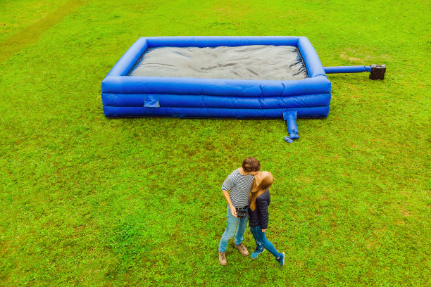 一对性感的年轻夫妇在绿色草地上一个巨大的蓝色充气蹦床的背景上图片下载
