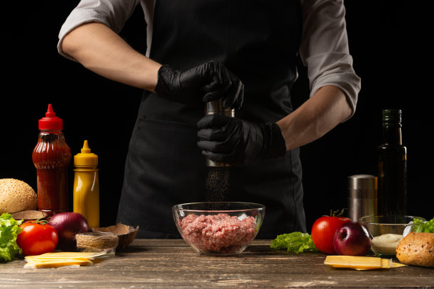 厨师用新鲜绞碎的牛肉来做汉堡中的肉饼。背景是汉堡的配料。水平的照片。烹饪美味的食物图片下载