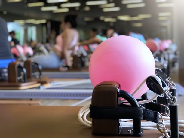 近距离的粉红球在普拉提改革者的床上，模糊的背景下，在健身房锻炼的妇女。生活健身，室内健身，健康理念图片下载