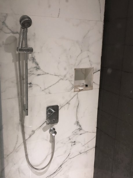 银色不锈钢墙淋浴装置和豪华浴室套房的软管，肥皂和洗发水的架子，与白色印度大理石瓷砖和对比鲜明的黑色瓷砖的照片图片下载