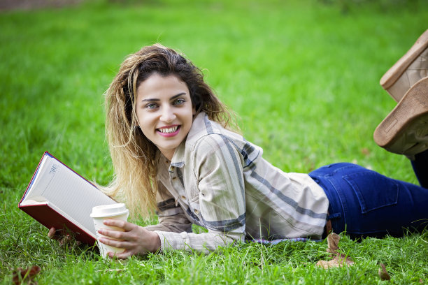 女人躺下或放松在绿色草地上阅读议程。图片下载