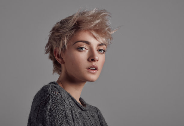 年轻女子的肖像在短短的金发穿美利奴羊毛毛衣孤立的灰色背景图片下载