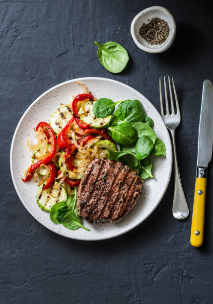 牛排与烤蔬菜，甜椒，西葫芦和新鲜菠菜在一个黑暗的背景，俯视图。美味健康均衡的午餐图片下载