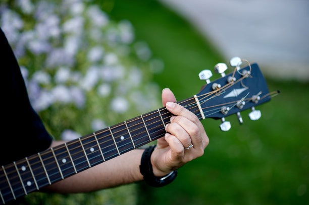 一个吉他手的图片，一个年轻人坐在一个自然的花园里弹吉他，音乐的概念图片下载