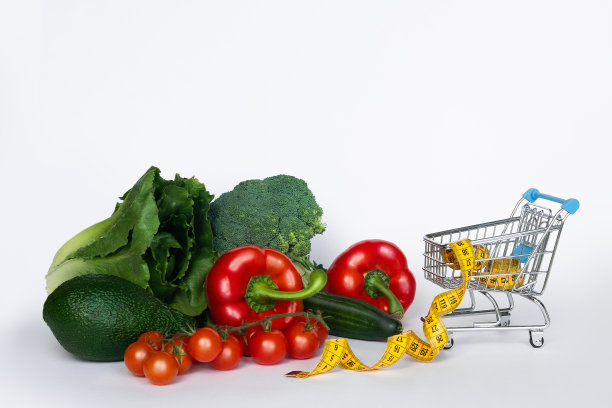 饮食的概念。购物车里的新鲜蔬菜和黄色的卷尺。健康的食物和适当的营养。正确的饮食概念。图片下载