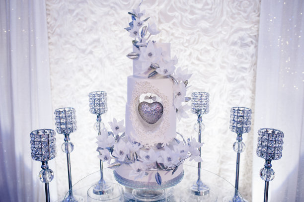 桌子上有婚礼蛋糕，蜡烛和鲜花。照片墙、婚庆装饰空间或场所从白色和银色风格。图片下载