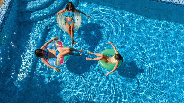 家庭在游泳池空中无人机从上面看，快乐的母亲和孩子游泳在充气圈甜甜圈和有乐趣的家庭度假，热带度假度假胜地图片下载