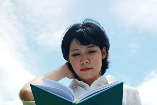 美丽的女人阅读和持有的书在天空的背景。图片下载