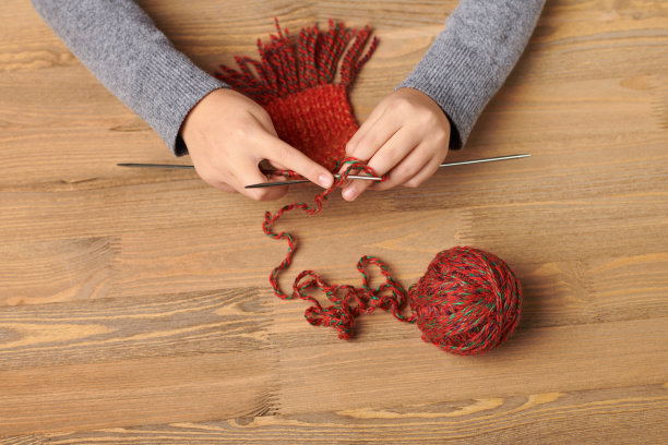 那个小女孩正在学织围巾。红色的毛线在木桌上。手的特写镜头。图片下载