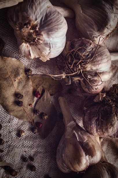 照片上是黑胡椒，月桂叶，大蒜的果实散落在织物上图片下载