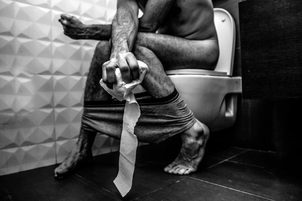 无色的灰色图像。在厕所里坐在马桶上很痛苦。他有便秘和痛苦。他用力捏着卫生纸。痛苦的和坏的。苍白的生病的人。图片下载