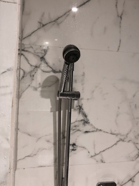 豪华浴室套房中银色不锈钢墙淋浴装置和软管的图像，与白色印度大理石瓷砖的照片图片下载
