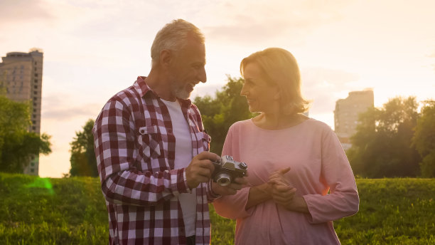 一对退休老人看着镜头上的照片，互相微笑，约会图片下载