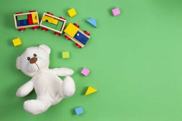 婴儿玩具背景。白色的泰迪熊，木制的玩具火车和绿色背景的彩色积木。俯视图，平放图片下载