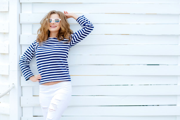 一张街景照片上，一名年轻的黑发女子站在浅蓝色的木栅栏旁，在空白的白色背景下向一边张望。水平模型。空白的文字设计空间。图片下载