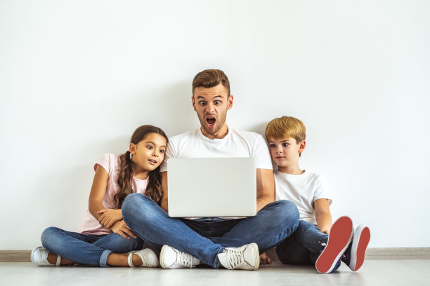 父亲和孩子们拿着笔记本电脑坐在地板上图片下载