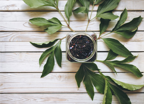 玻璃杯中的干红茶，木色背景，牡丹绿叶。图片下载