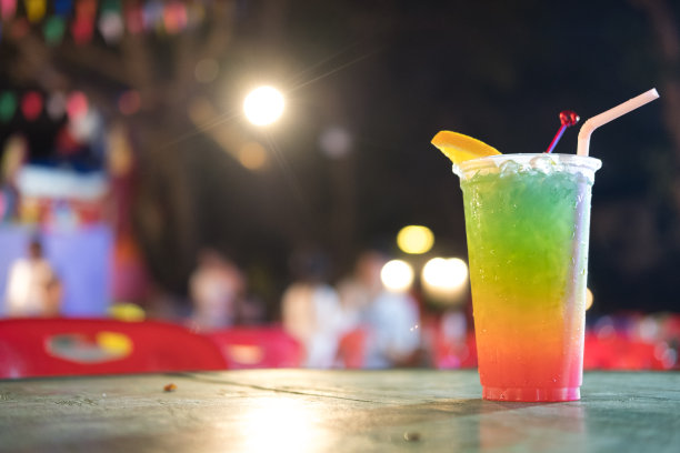 晚上的咖啡馆里，鲜亮的水果鸡尾酒和一片橙色的塑料杯。夏天水果饮料图片下载