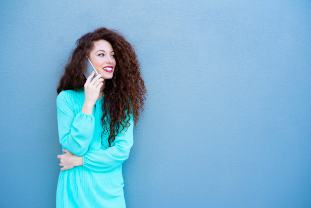 快乐的年轻女子在手机旁一堵彩色的墙图片下载