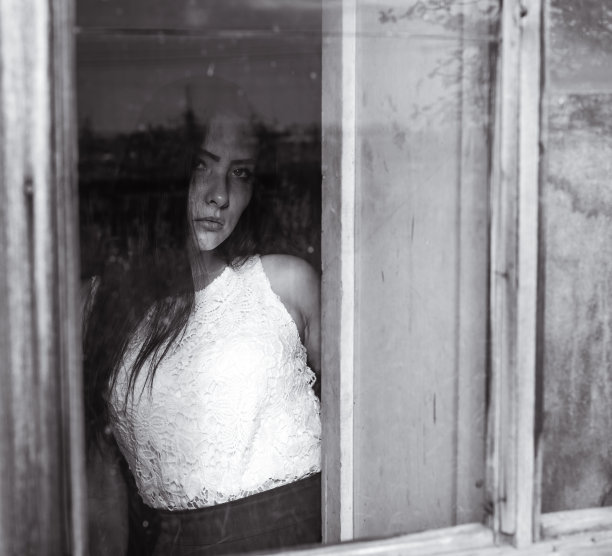 小女孩坐在窗边的木屋里，昏暗的黑白色彩图片下载