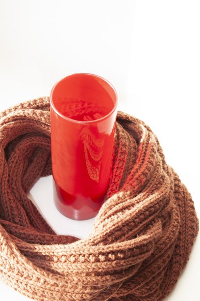 一个红色的玻璃花瓶和一条编织的棕色围巾。装饰背景图片下载