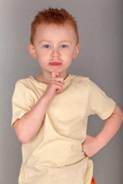 炽热的红头发的年轻男孩在黄色衬衫在手指到下巴在肖像格式与副本空间灰色背景上沉思的立场。隐喻思维。表情包和可爱红头发的海报图片。图片下载