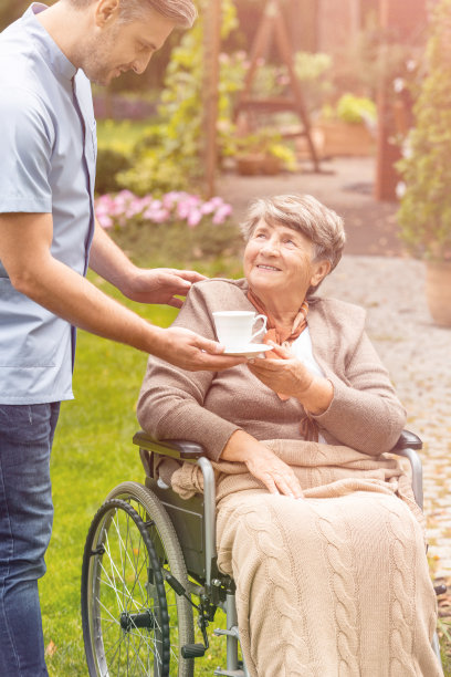 坐在轮椅上的老妇人向护士端着一杯茶图片下载