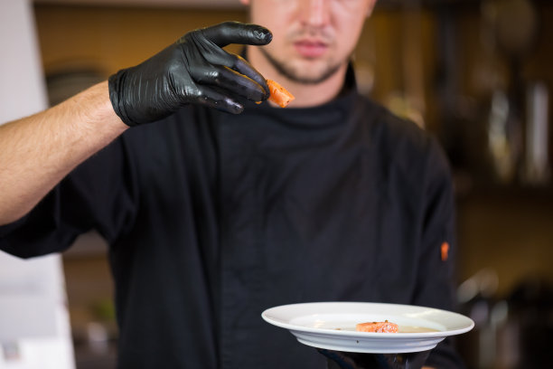 主题烹饪是烹饪的专业。白人男子的肖像在餐厅厨房准备红色鱼片鲑鱼肉在黑色手套制服。厨师拿着蓝色的盘子，检查味道图片下载