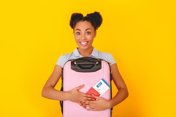 年轻的非洲女人孤立在黄色的墙壁工作室可爱的风格旅行者抱着行李的概念图片下载