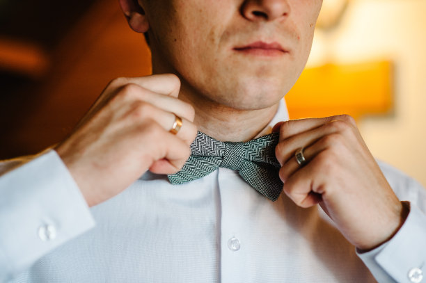 一个男人的时尚照片，男人的手触摸领结在西装纠正他的领结。早上准备在家梳妆。图片下载