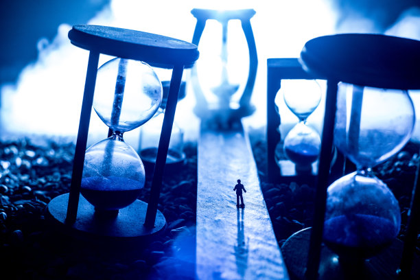 时间的概念。一个男人的剪影站在沙漏中间，在黑暗的背景上有烟雾和灯光。超现实主义的装修图片图片下载