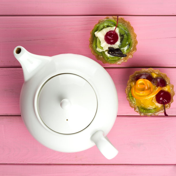 五颜六色的水果蛋糕由奇异果、橘子、蜜饯樱桃、奶油和巧克力在粉红色的背景和一个茶壶。图片下载