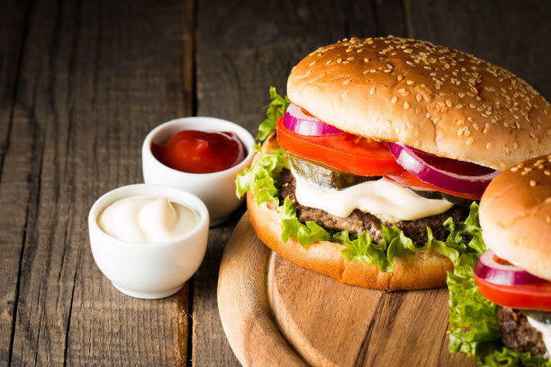 自制汉堡的特写照片，啤酒由牛肉、洋葱、番茄、生菜、奶酪和香料制成。新鲜的汉堡特写在木制的乡村桌子和土豆薯条和薯条。图片下载
