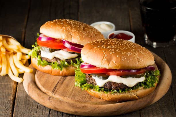自制汉堡的特写照片，啤酒由牛肉、洋葱、番茄、生菜、奶酪和香料制成。新鲜的汉堡特写在木制的乡村桌子和土豆薯条和薯条。图片下载
