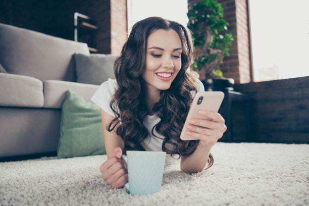 近距离的照片可爱的漂亮的黑发的她她的夫人，电话，手，手臂，热饮料，写信，穿着运动服，浅色的t恤，裤子，衣服，躺着地毯，地板，沙发图片下载