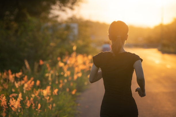 年轻的健身运动女子在清晨的马路上跑步，阳光耀斑图片下载