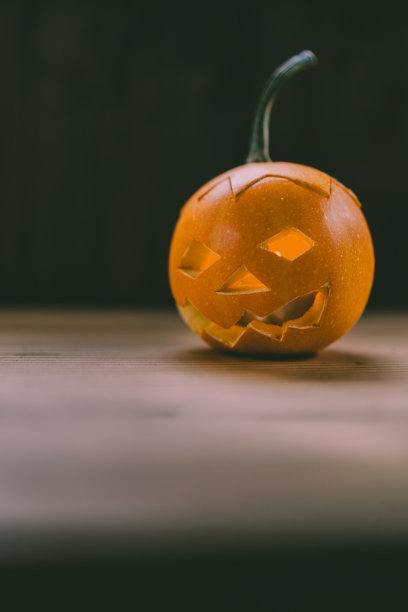 雕刻婴儿南瓜的特写照片在木制的背景与蜡烛光手套眼睛和嘴-孤立的对象模糊的背景，万圣节节日广告材料图片下载