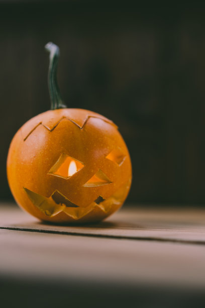雕刻婴儿南瓜的特写照片在木制的背景与蜡烛光手套眼睛和嘴-孤立的对象模糊的背景，万圣节节日广告材料图片下载