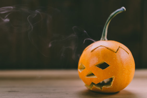 雕刻婴儿南瓜的特写照片在木制的背景与蜡烛光手套眼睛和嘴-孤立的对象模糊的背景，万圣节节日广告材料图片下载