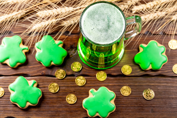 玻璃杯里的绿色啤酒、姜饼三叶草、马蹄铁、麦穗和金币放在粗糙的木头表面上。圣帕特里克节的节日背景。图片下载