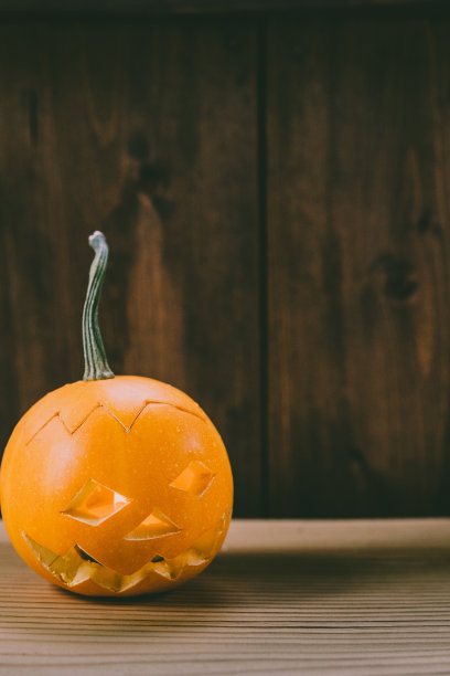 雕刻婴儿南瓜的特写照片在木制的背景与蜡烛光手套眼睛和嘴-孤立的对象模糊的背景，万圣节节日广告材料图片下载