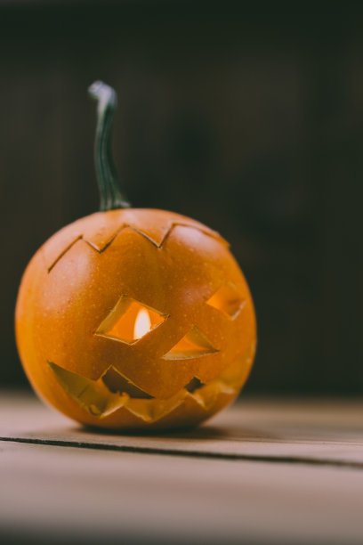 雕刻婴儿南瓜的特写照片在木制的背景与蜡烛光手套眼睛和嘴-孤立的对象模糊的背景，万圣节节日广告材料图片下载