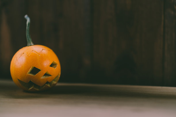 雕刻婴儿南瓜的特写照片在木制的背景与蜡烛光手套眼睛和嘴-孤立的对象模糊的背景，万圣节节日广告材料图片下载