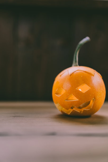 雕刻婴儿南瓜的特写照片在木制的背景与蜡烛光手套眼睛和嘴-孤立的对象模糊的背景，万圣节节日广告材料图片下载
