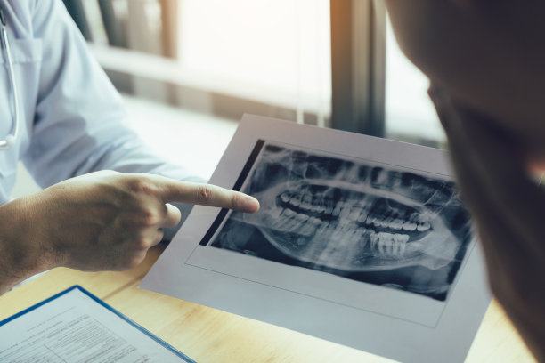 牙科医生用手指着x光片，并与病人谈论药物和手术治疗。图片下载