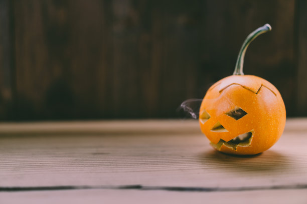 雕刻婴儿南瓜的特写照片在木制的背景与蜡烛光手套眼睛和嘴-孤立的对象模糊的背景，万圣节节日广告材料图片下载