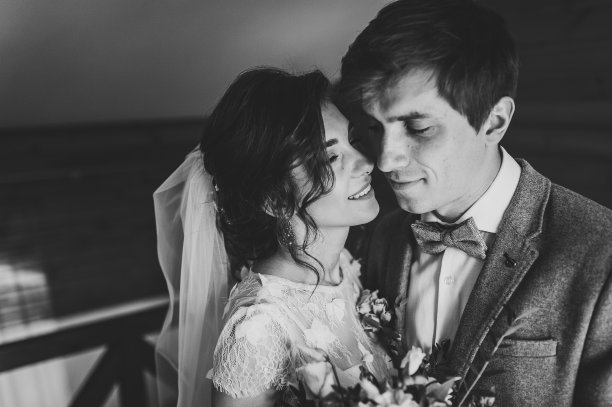 穿着西装的新郎在家里拥抱着穿着白色婚纱的新娘，手里捧着美丽的婚礼花束。一对美丽的年轻夫妇的肖像。黑白照片。图片下载