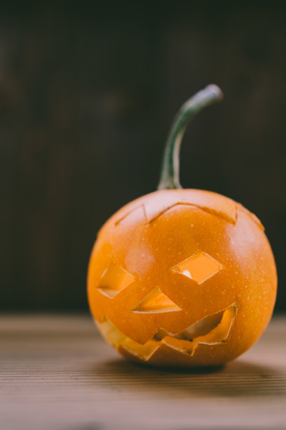 雕刻婴儿南瓜的特写照片在木制的背景与蜡烛光手套眼睛和嘴-孤立的对象模糊的背景，万圣节节日广告材料图片下载