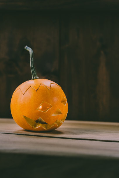 雕刻婴儿南瓜的特写照片在木制的背景与蜡烛光手套眼睛和嘴-孤立的对象模糊的背景，万圣节节日广告材料图片下载